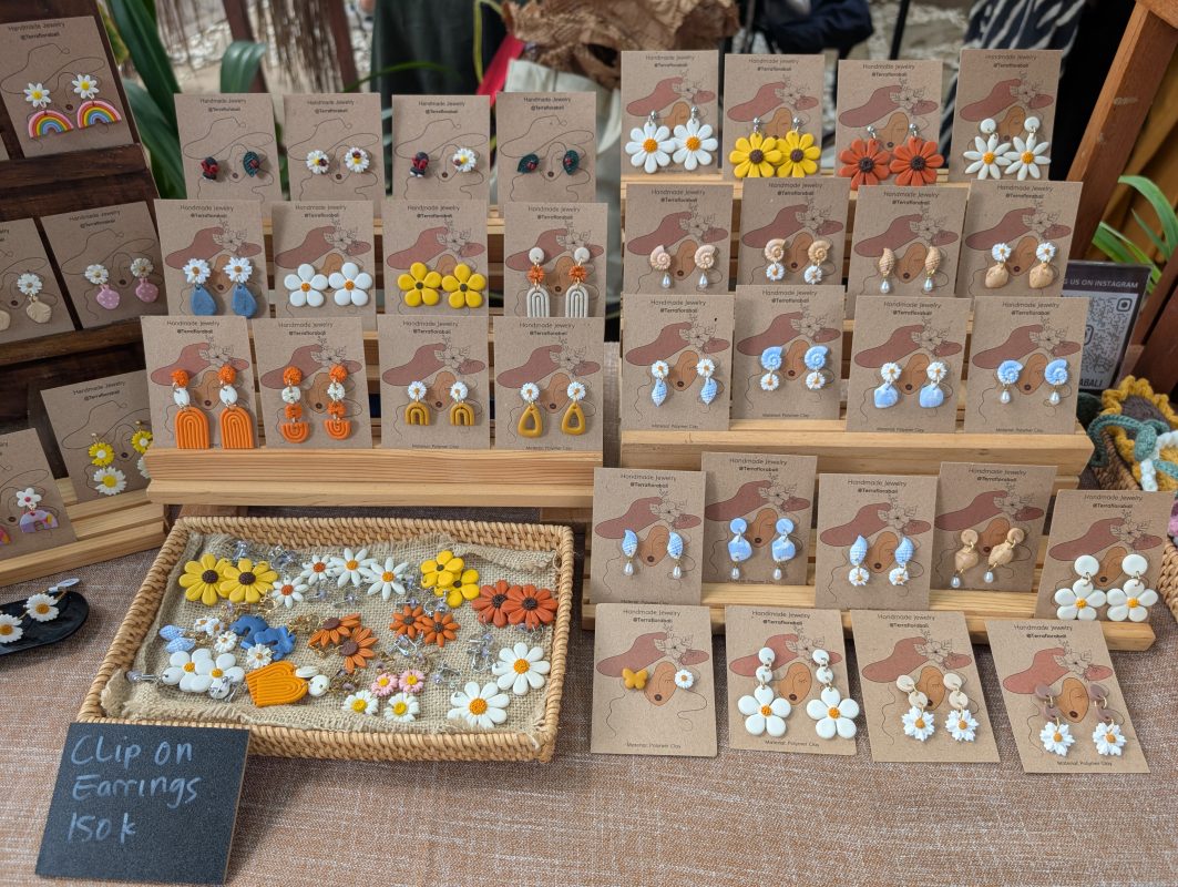 Tiered wooden racks of handmade clay earrings on kraft cards at the Terra Flora Bali market stall