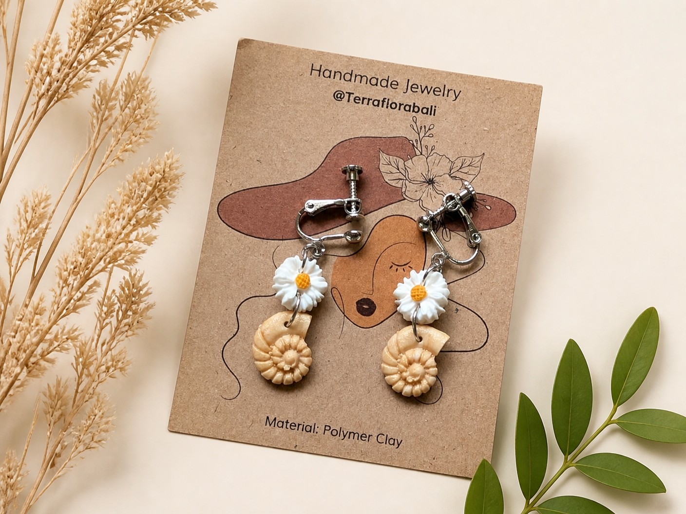 Handmade clay clip-on earrings with a white daisy above a cream spiral shell on a kraft card